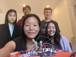 PXL_20210728_191648124 A group of five young people smiling, with an electronic project involving wires and sensors in the foreground.