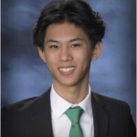 Evoto-5.1.0-351 A headshot of a person wearing a black suit, white shirt, and green tie, smiling against a blurred blue background.
